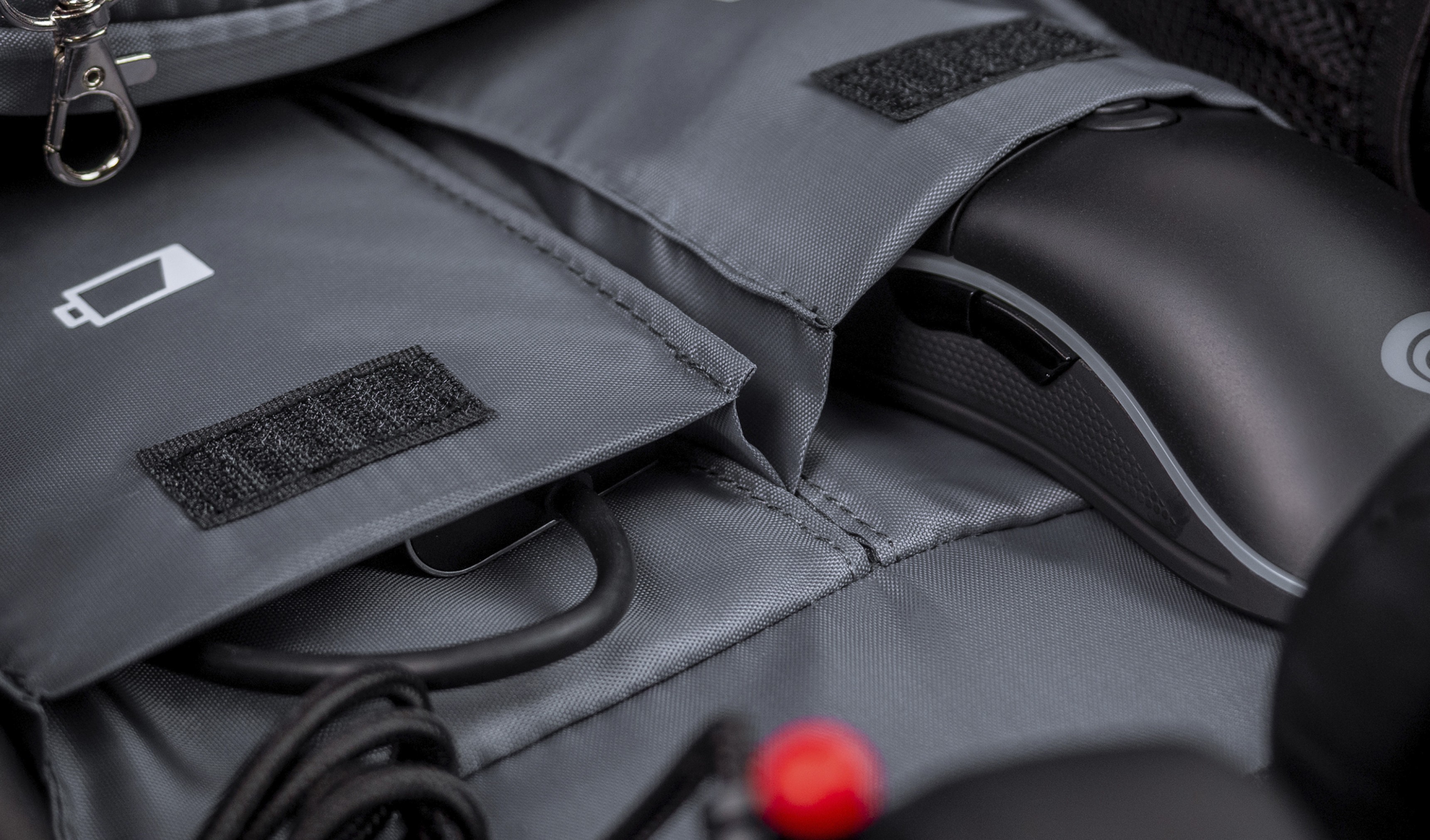 Intérieur gris du sac à dos Genesis Pallad 550, montrant des compartiments pour une souris et des câbles, avec une icône de batterie visible.