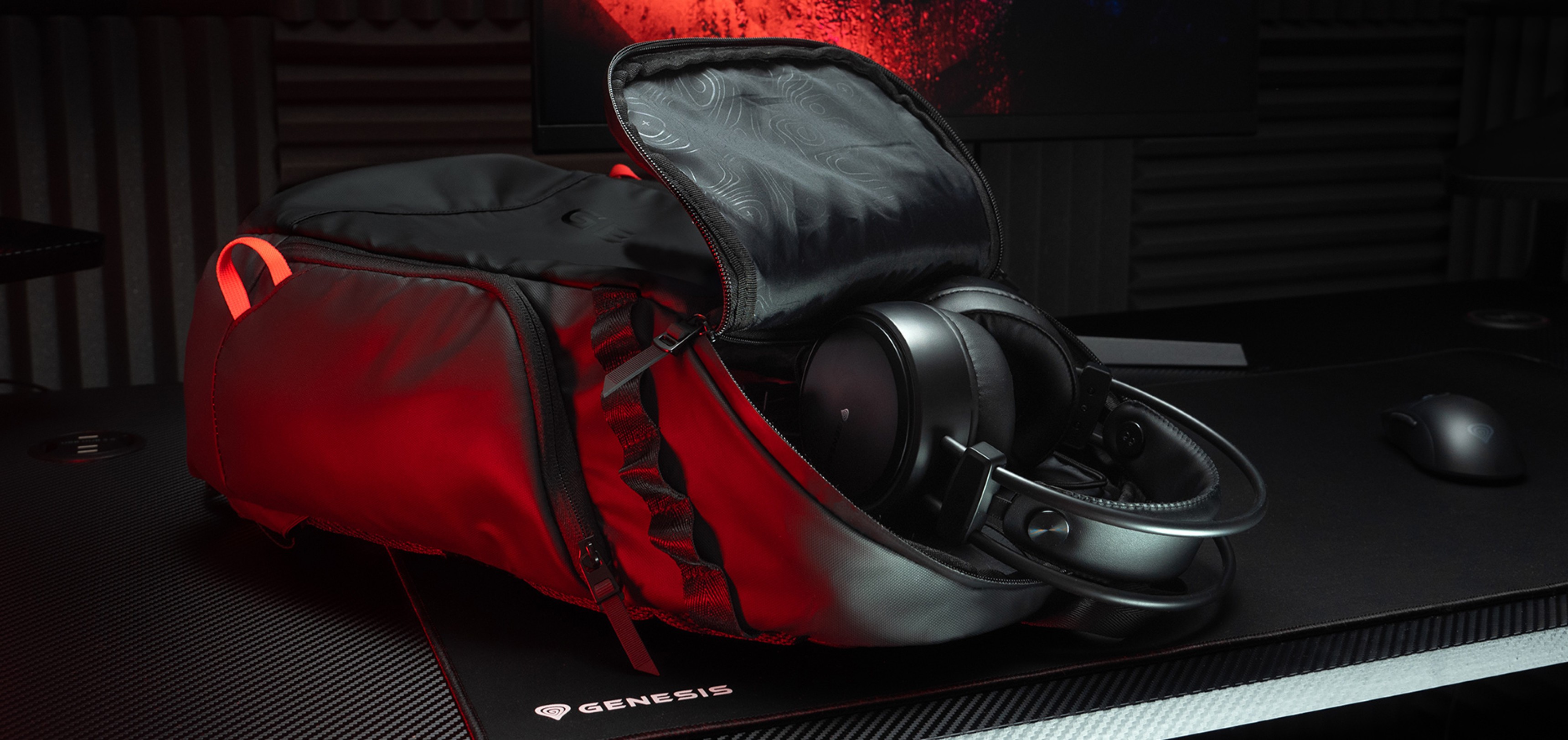 Sac à dos pour ordinateur portable Genesis Pallad noir avec un compartiment partiellement ouvert et des écouteurs à l'intérieur, posé sur un bureau texturé.