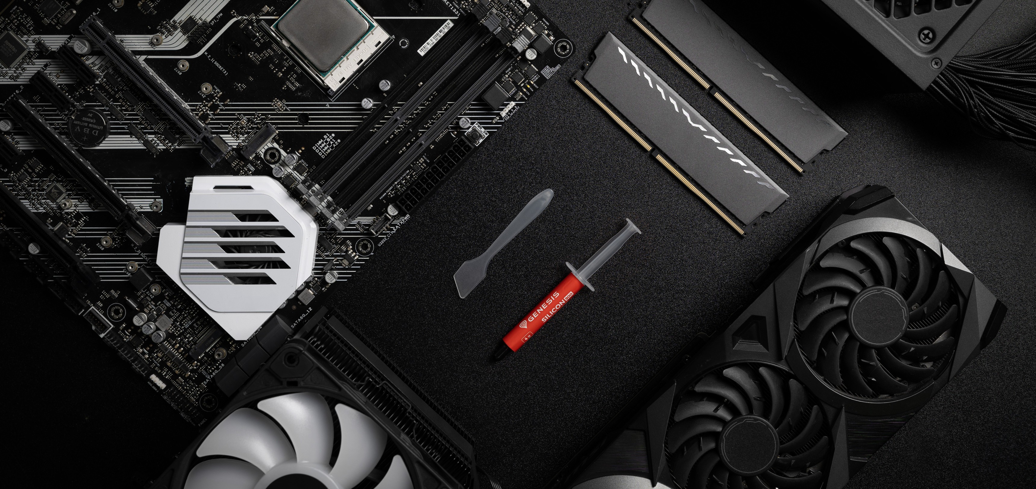 Tube de pâte thermique avec une spatule, placé sur un fond noir à côté d'une carte mère, d'une mémoire vive et d'un GPU.