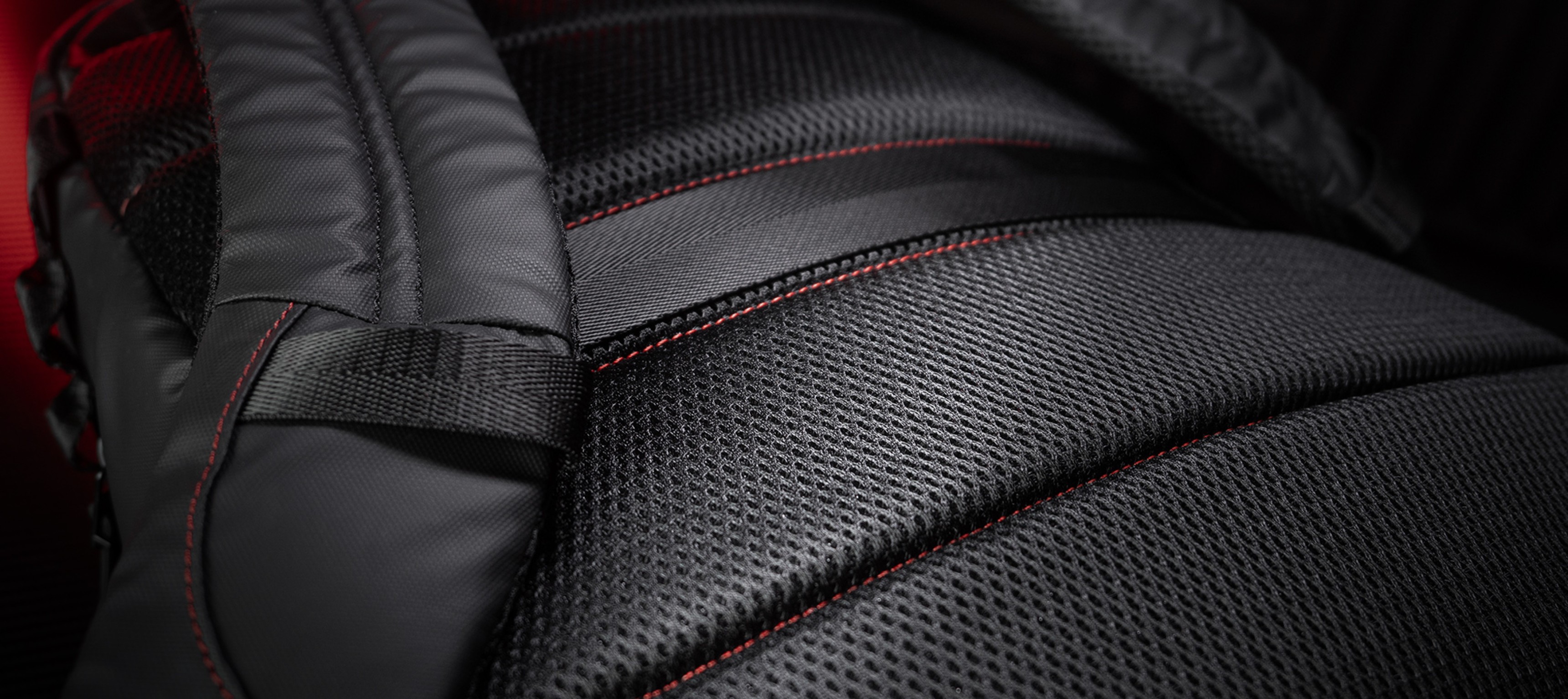 Gros plan sur le sac à dos Genesis Pallad 420, mettant en valeur son tissu noir texturé avec des coutures rouges et des bretelles rembourrées.
