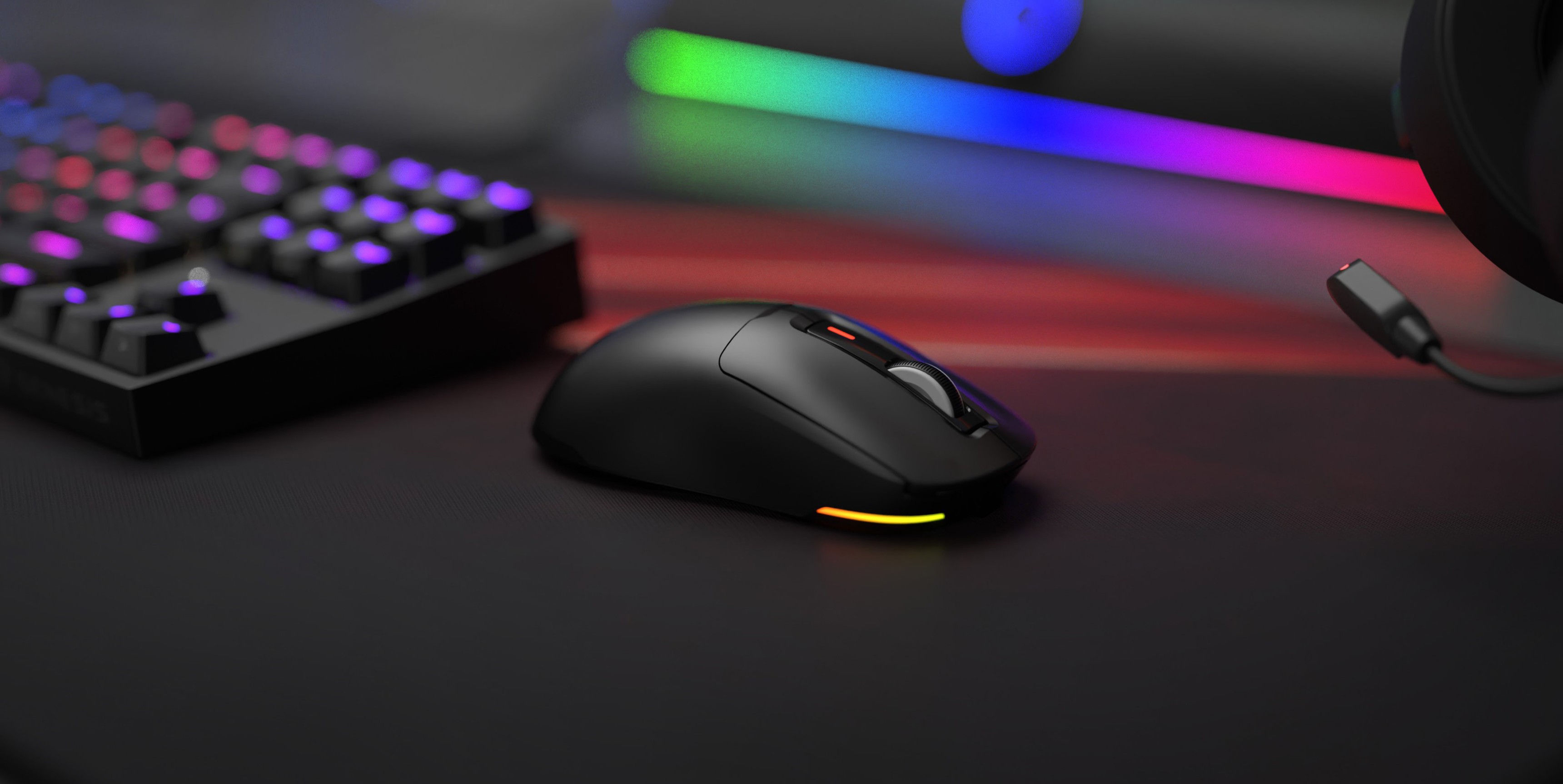 Souris de jeu sans fil Genesis Zircon 660 noire avec éclairage RVB, placée sur un bureau de jeu élégant aux côtés d'un clavier mécanique.