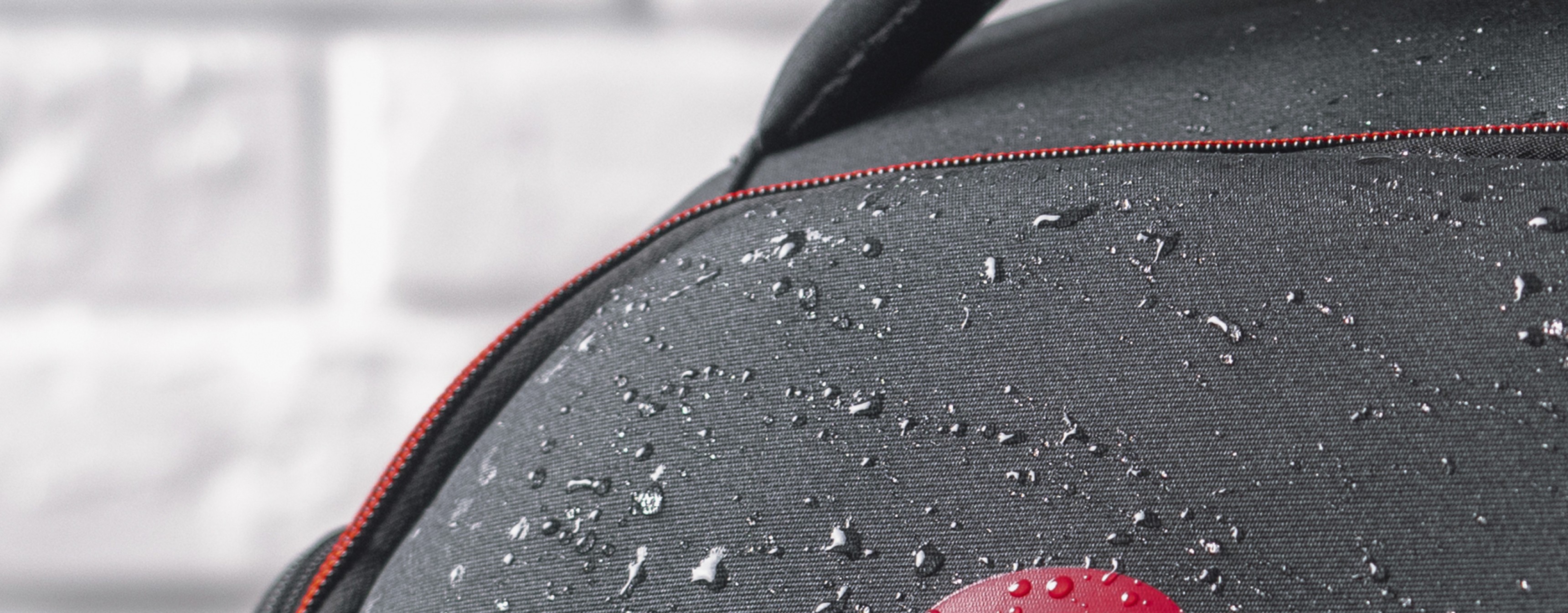 Sac à dos pour ordinateur portable noir résistant à l'eau avec des accents rouges, adapté aux ordinateurs portables de 15,6"/17,3", montrant des gouttelettes sur le tissu.