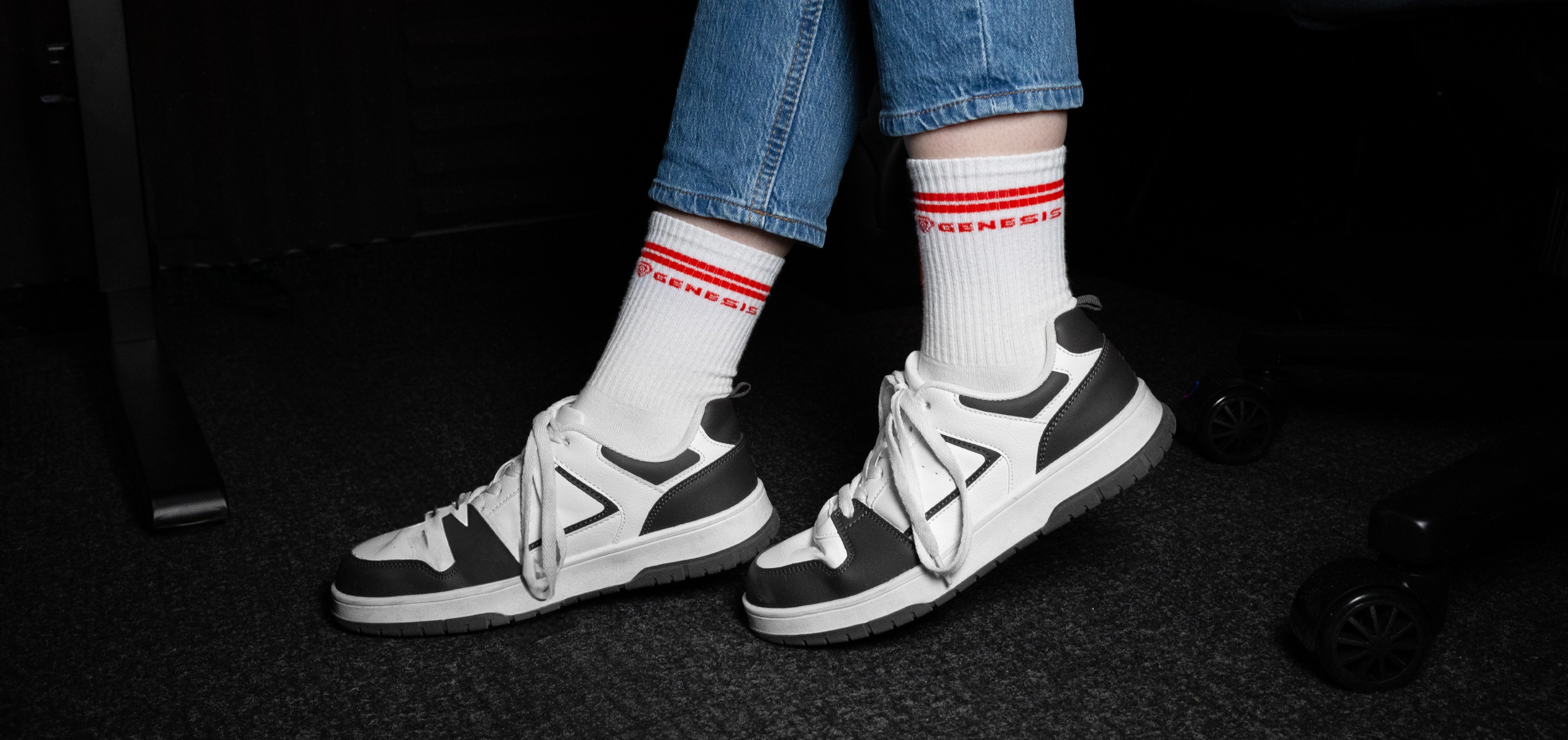 Chaussettes de sport en blanc avec des rayures rouges, associées à des baskets grises et blanches et à un jean bleu.