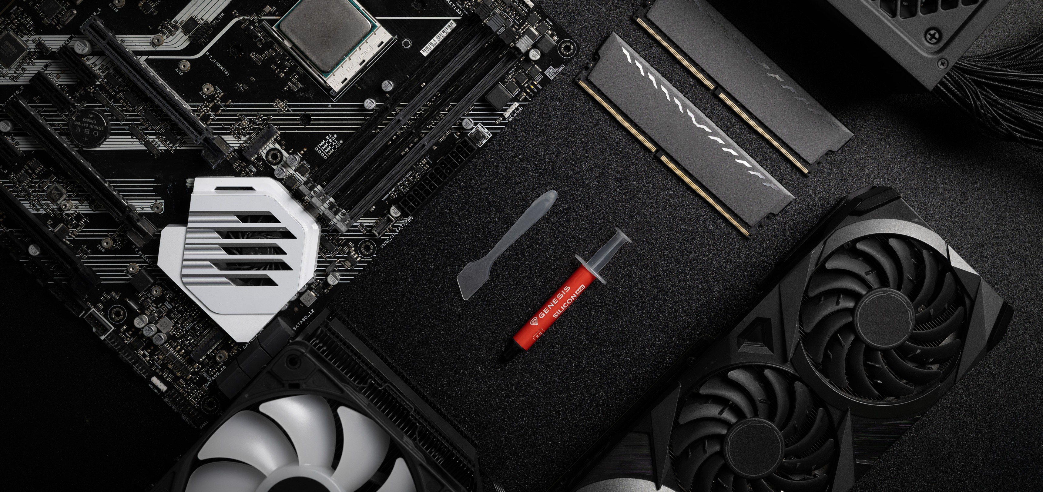 Tube de pâte thermique avec une spatule présenté sur une carte mère, à côté des composants de la RAM et du GPU.